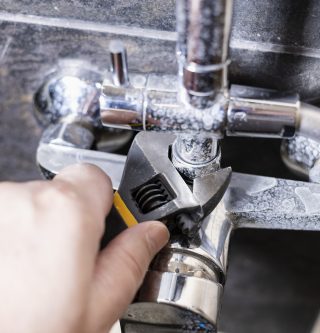 plumber fixes nut of shower faucet close up on tiled wall at home